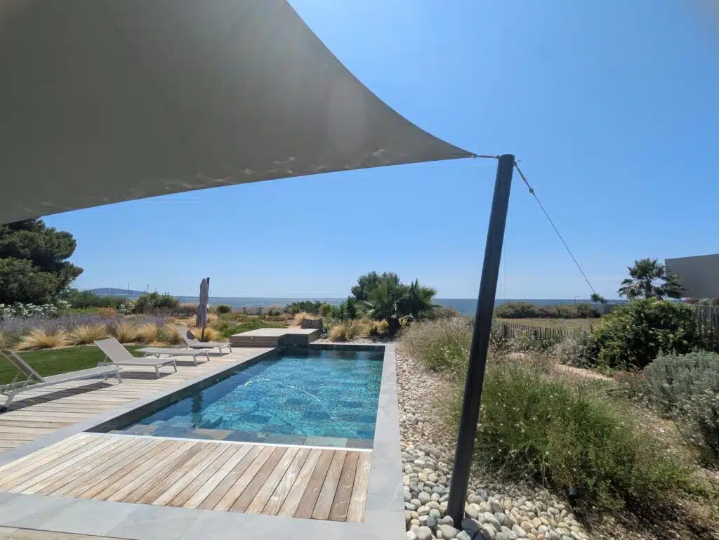 Voile 6 pointes Soltis 92 vert de gris au-dessus d’une piscine avec vue sur l’étang de Thau à Mèze.